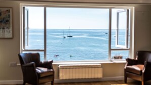 A room with a large window overlooking a calm sea with boats. There are two leather chairs and a radiator below the window. - 3 Beach Way House (Lyme Regis)