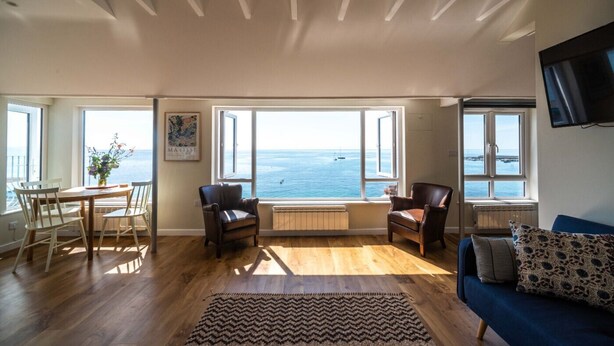 A spacious living room with a view of the sea, wooden flooring, a dining table with chairs, and a blue sofa. - 3 Beach Way House (Lyme Regis)