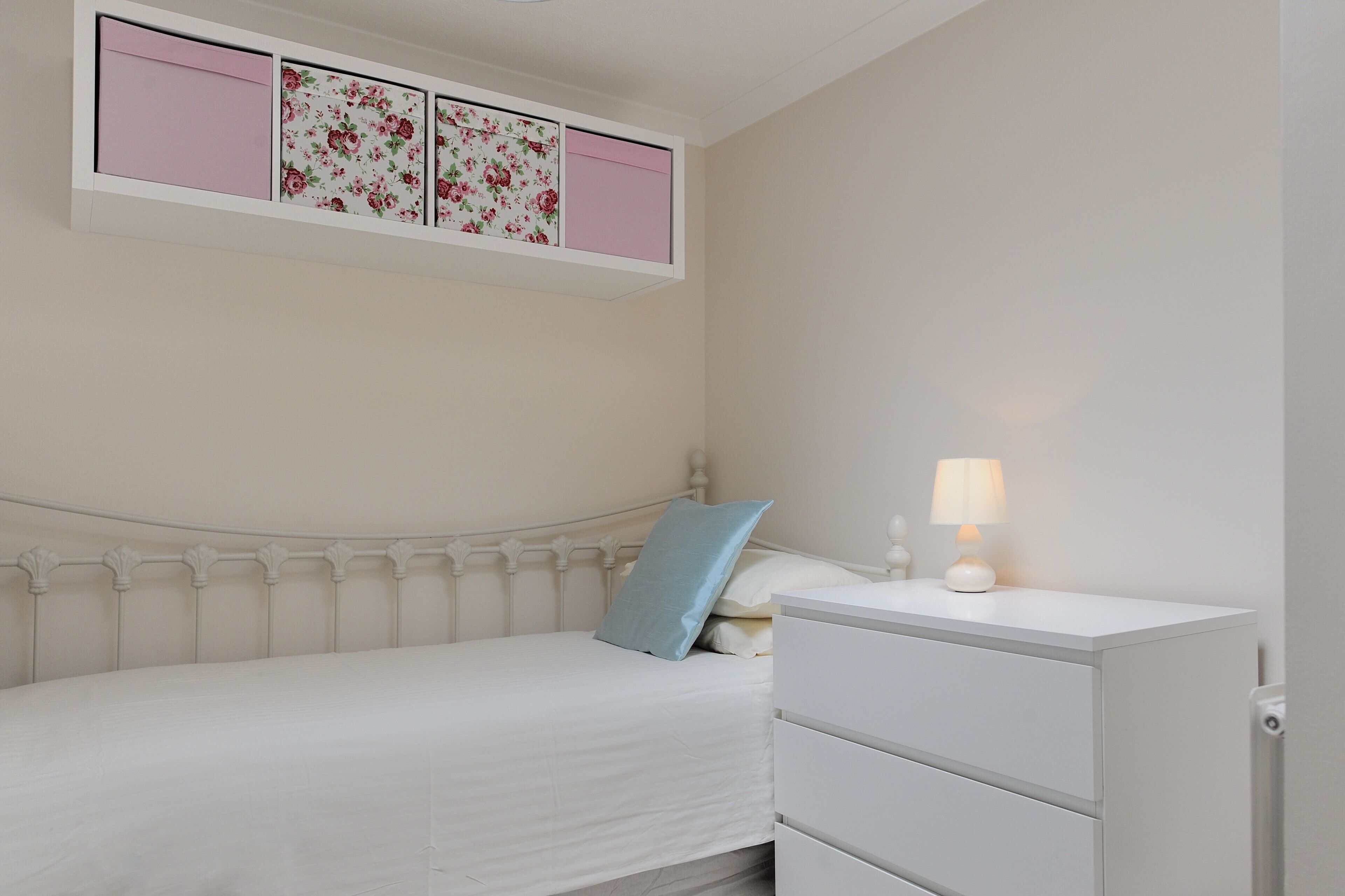 Ein Schlafzimmer mit Bett, Nachttisch mit Lampe und Wandregal mit floralem Wandpapier.