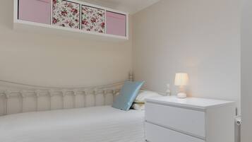 Ein Schlafzimmer mit Bett, Nachttisch mit Lampe und Wandregal mit floralem Wandpapier.