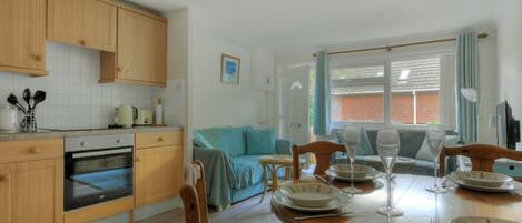 A kitchen with wooden cabinets, a dining table set for four, and a blue sofa in the background.