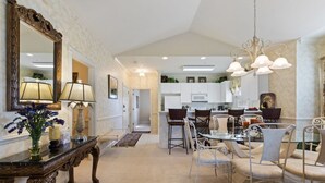 A spacious dining area with a glass table and white chairs, a large ornate mirror, and a chandelier. - Stunning 3BR Condo Magnolia Point (Myrtle Beach)