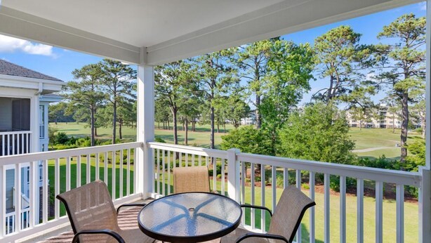 A covered outdoor area with a table and chairs, a white railing, and a view of a golf course. - Stunning 3BR Condo Magnolia Point (Myrtle Beach)