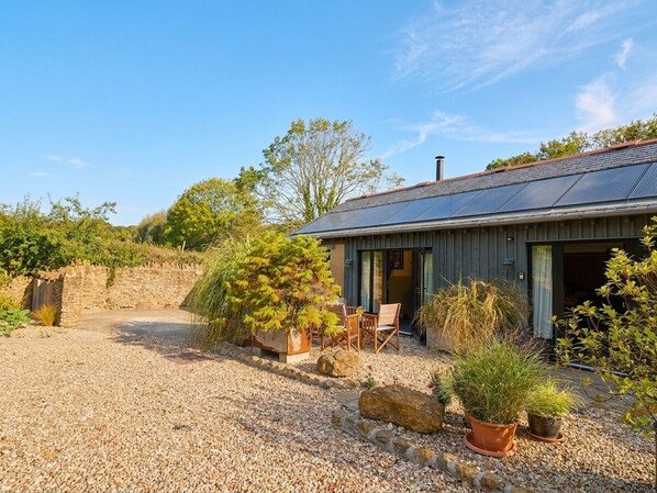 A rustic building with a gravel driveway, outdoor seating, and solar panels on the roof.