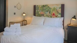 A neatly made bed with white linens, a painting above it, and two bedside lamps.