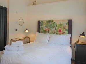 Un lit bien fait, avec du linge de lit blanc, un tableau au-dessus et deux lampes de chevet.