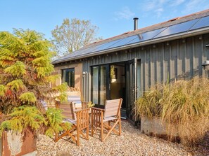A modern building with a sloped roof, solar panels, and a patio area with wooden furniture.