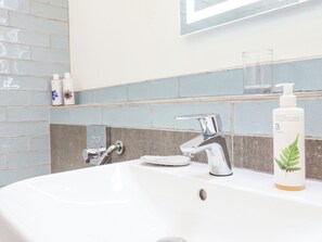 A bathroom with a white sink, chrome faucet, and a bottle of hand wash soap.