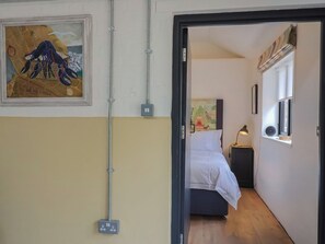 A bedroom with a bed, bedside table, lamp, and a painting on the wall.