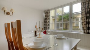 A dining table set with white plates, bowls, and wine glasses, with a window view and curtains. - Tudor Cottage (Lyme Regis)