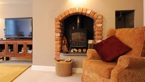A living room with a brick fireplace, a television, and a patterned sofa. - Tudor Cottage (Lyme Regis)