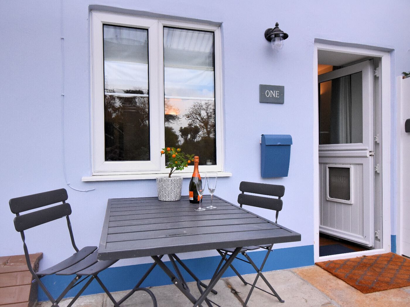 A table with four chairs, a potted plant, a bottle, and a glass on the windowsill.