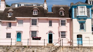 Une rangée de charmantes maisons de bord de mer aux toits de chaume, aux façades aux couleurs pastel et à l’escalier en pierre menant à l’entrée.