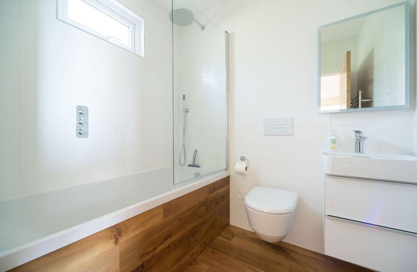 A modern bathroom with a glass-enclosed shower, a white toilet, and a wooden vanity with a mirror.