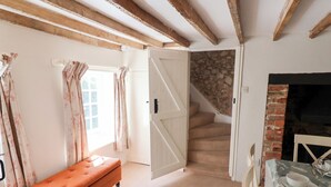 Una habitación con techo de madera, un banco, una mesa de comedor con platos y un vaso, y una escalera que conduce a una pared de piedra.