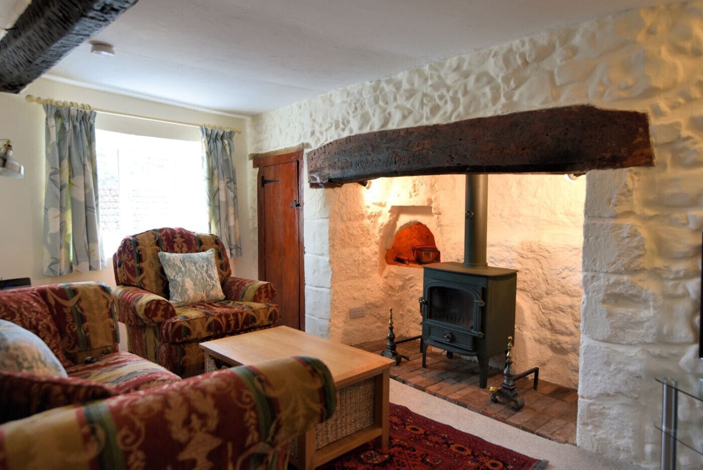 A cozy living room with a stone fireplace, patterned armchairs, and a wooden coffee table.