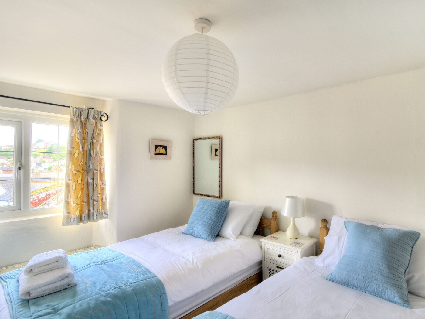 Une chambre avec deux lits, une fenêtre avec des rideaux, une lampe de chevet et un miroir fixé au mur.