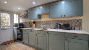 A kitchen with grey cabinets, a tiled backsplash, a built-in oven, and a window with a view. - Smugglers Cottage (Seaton)