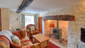 A cozy living room with a stone fireplace, patterned sofas, and a wooden coffee table. - Smugglers Cottage (Seaton)
