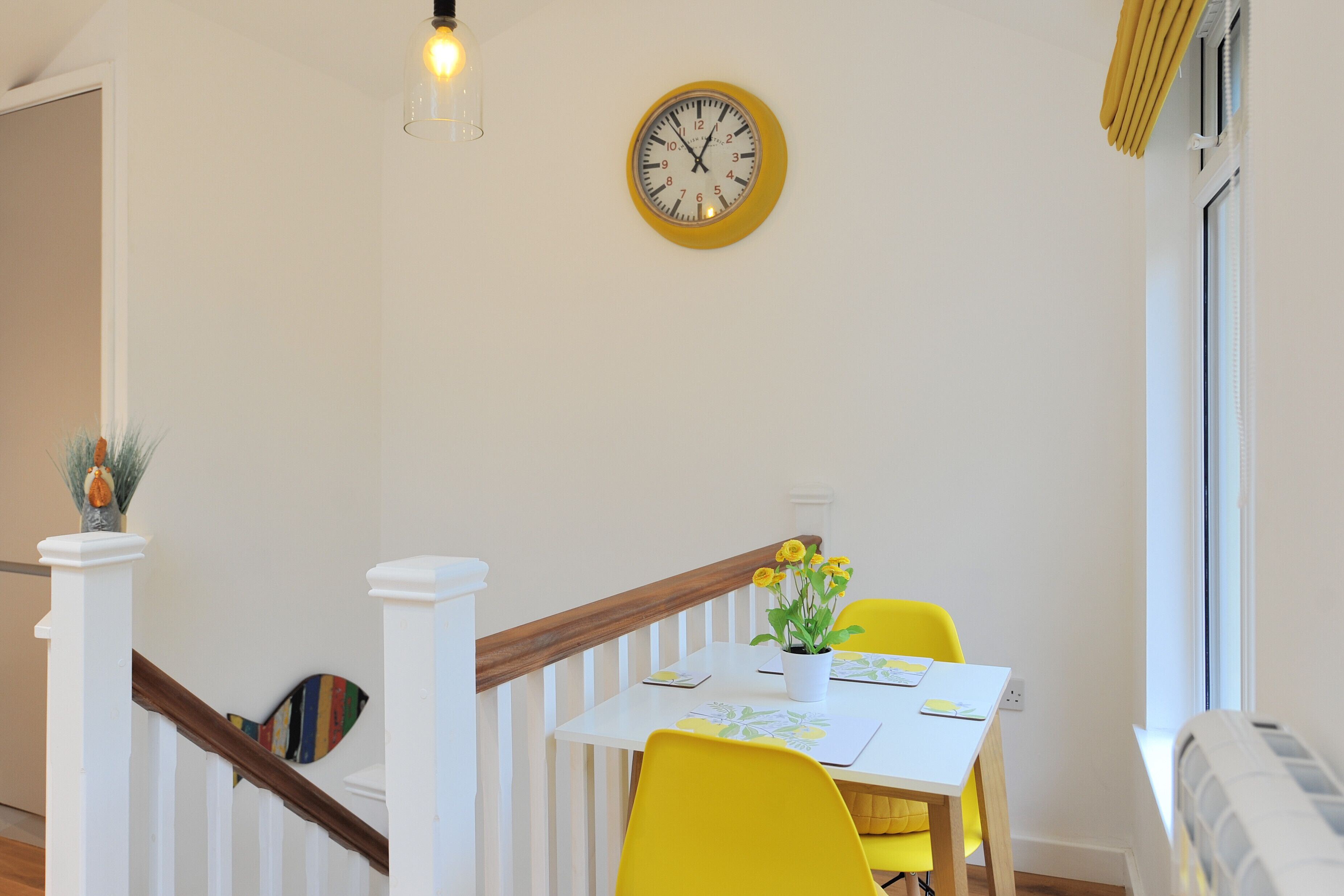 A dining area with a yellow table, chairs, and a clock on the wall.