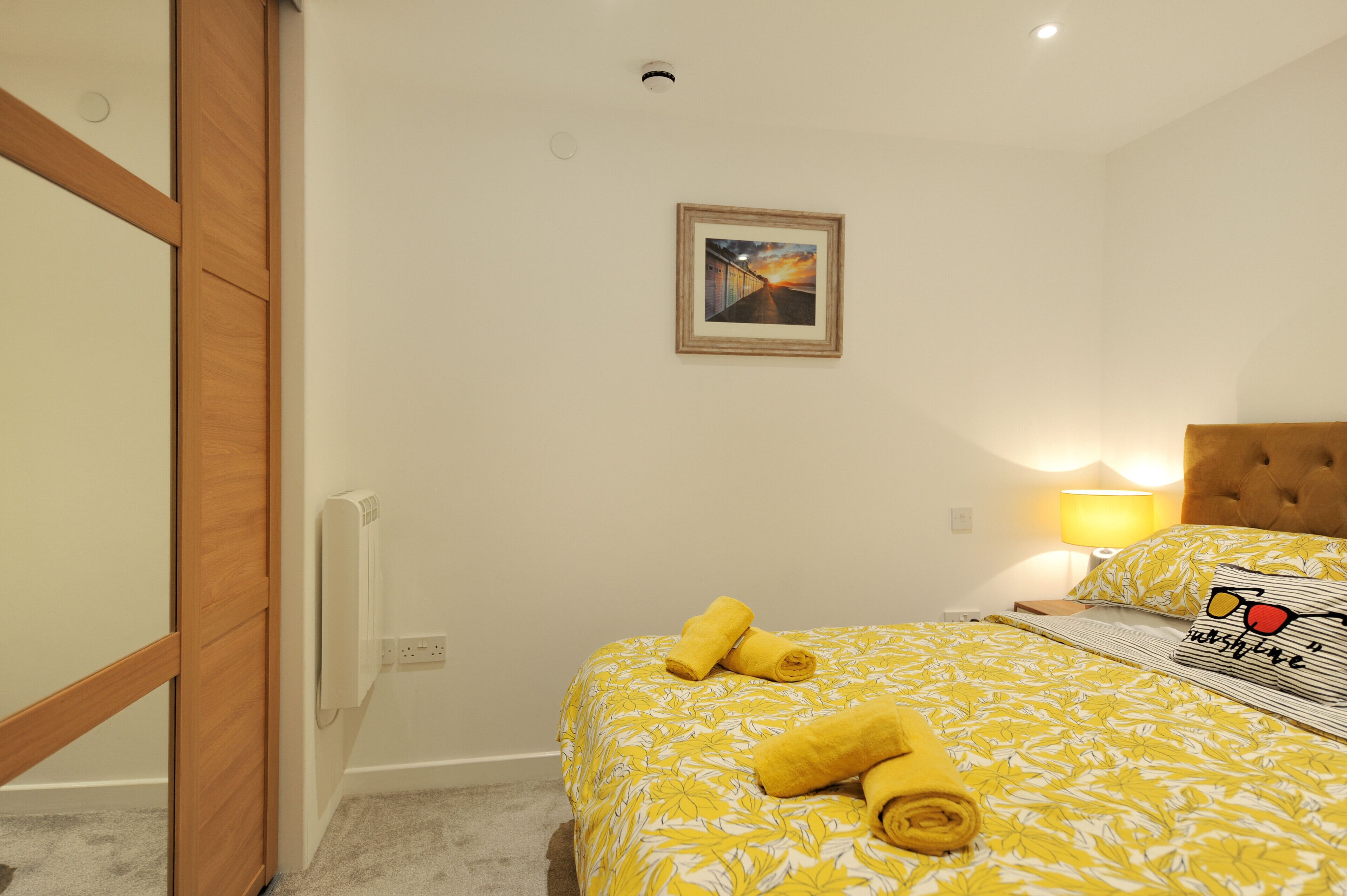 A bedroom with a bed, a nightstand, a lamp, and a painting on the wall.