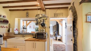 Een keuken met houten balken, een hangende kruidenrek en een magnetron op het aanrecht.
