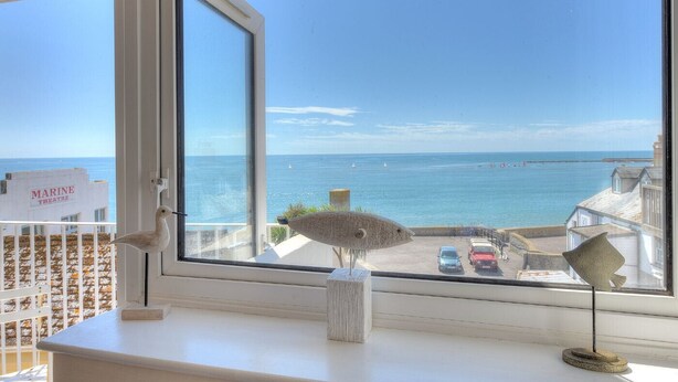 A view from a window overlooking a coastal area with a marina theatre sign, a beach, and a pier in the distance. - 6 Bay View Court (Lyme Regis)