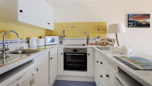 A compact kitchen with white cabinets, a microwave, a stove, and a sink. There is a small oven built into the cabinetry. - 6 Bay View Court (Lyme Regis)