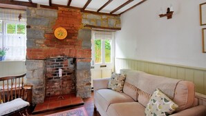 A cozy living room with a stone fireplace, a wooden bench, and a cushioned sofa with patterned cushions. - Lavender Cottage (Lyme Regis)