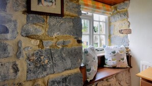 A stone-walled room with a window, a wooden bench, and a framed picture on the wall. - Lavender Cottage (Lyme Regis)