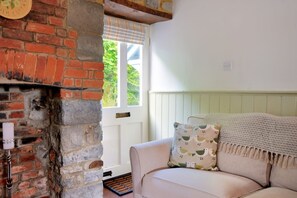 A cozy room with a brick fireplace, a white door, and a beige sofa with patterned cushions. - Lavender Cottage (Lyme Regis)
