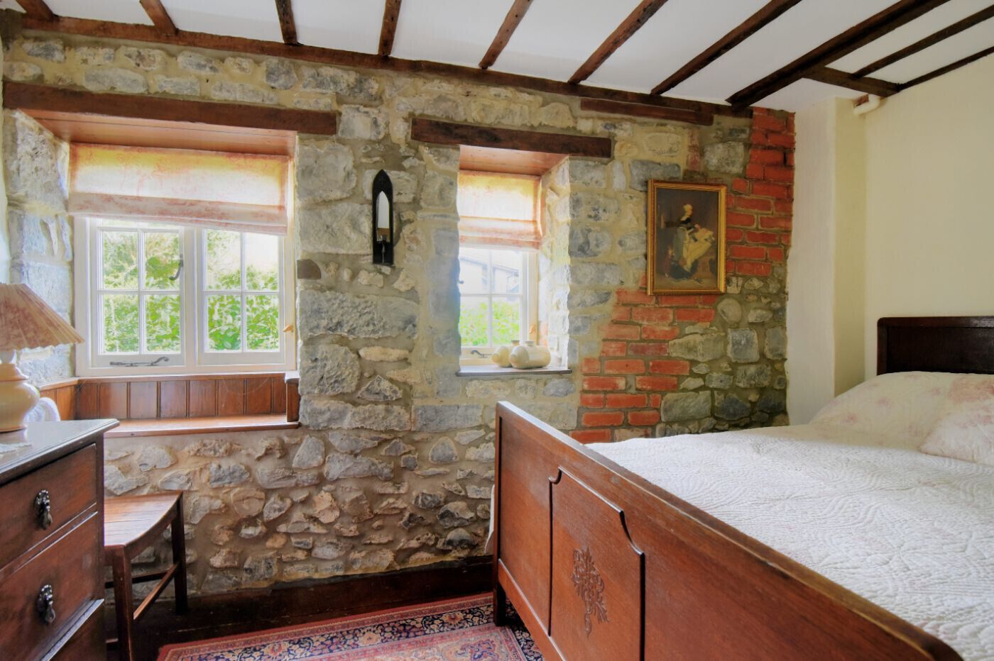 Een slaapkamer met een stenen muur, een houten bed en een raam met uitzicht op groen.