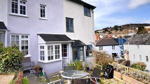 A two-story house with a white exterior and a small patio area with a table and chairs. - Lavender Cottage (Lyme Regis)