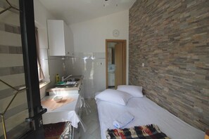 A compact hotel room with a kitchenette, a bed with white linens, and a stone-textured wall. - Little studio Sanjica in Pula, one person (Pula)