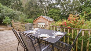 Une terrasse en bois avec une table dressée pour deux personnes, entourée d’une clôture en bois et d’une végétation luxuriante.