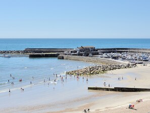 A coastal beach with a rocky breakwater, a marina with boats, and a building with a sloped roof. - The Stable (Lyme Regis)