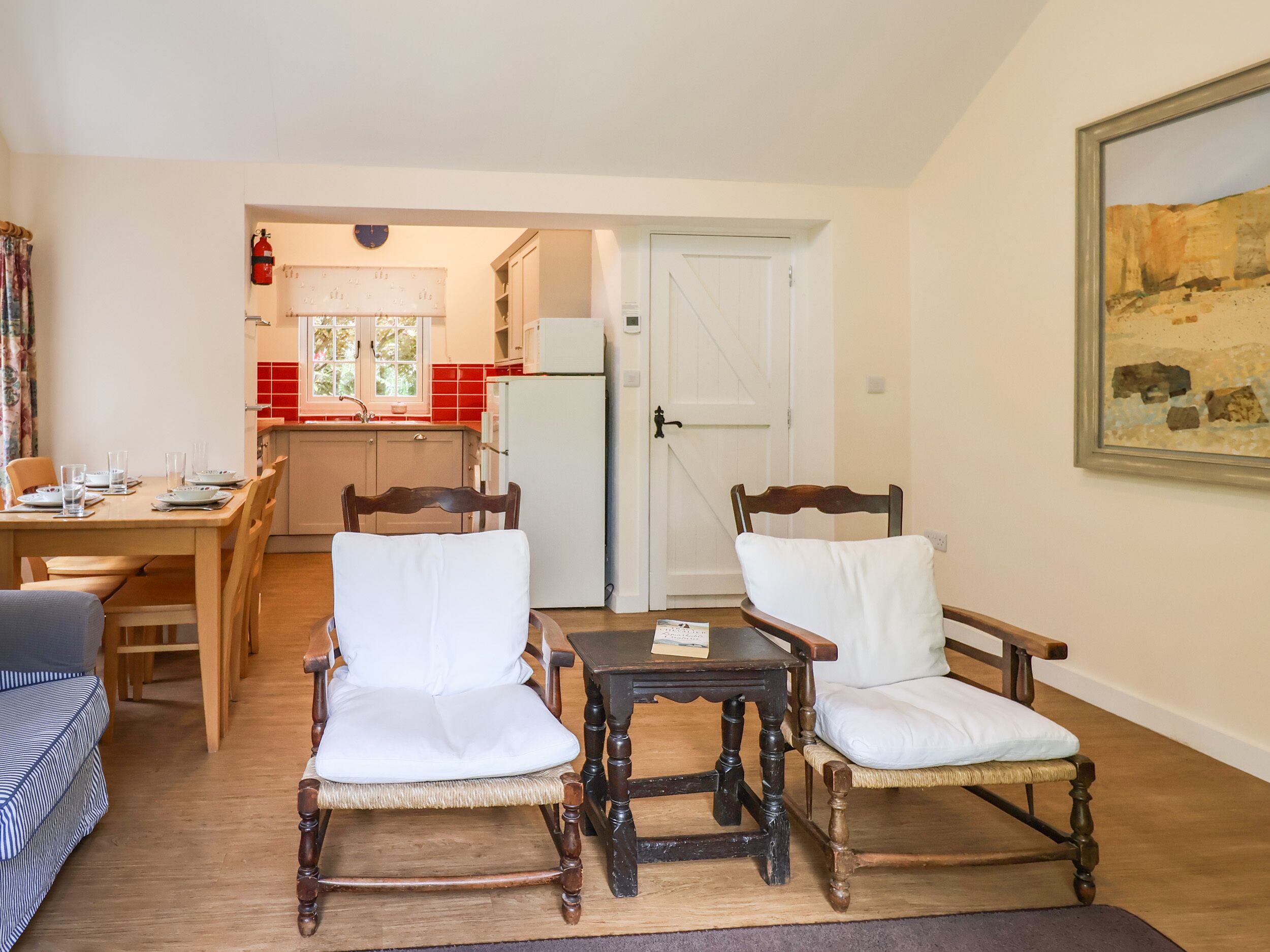 A dining area with two wooden chairs and a table, a kitchen in the background, and a door leading to another room.