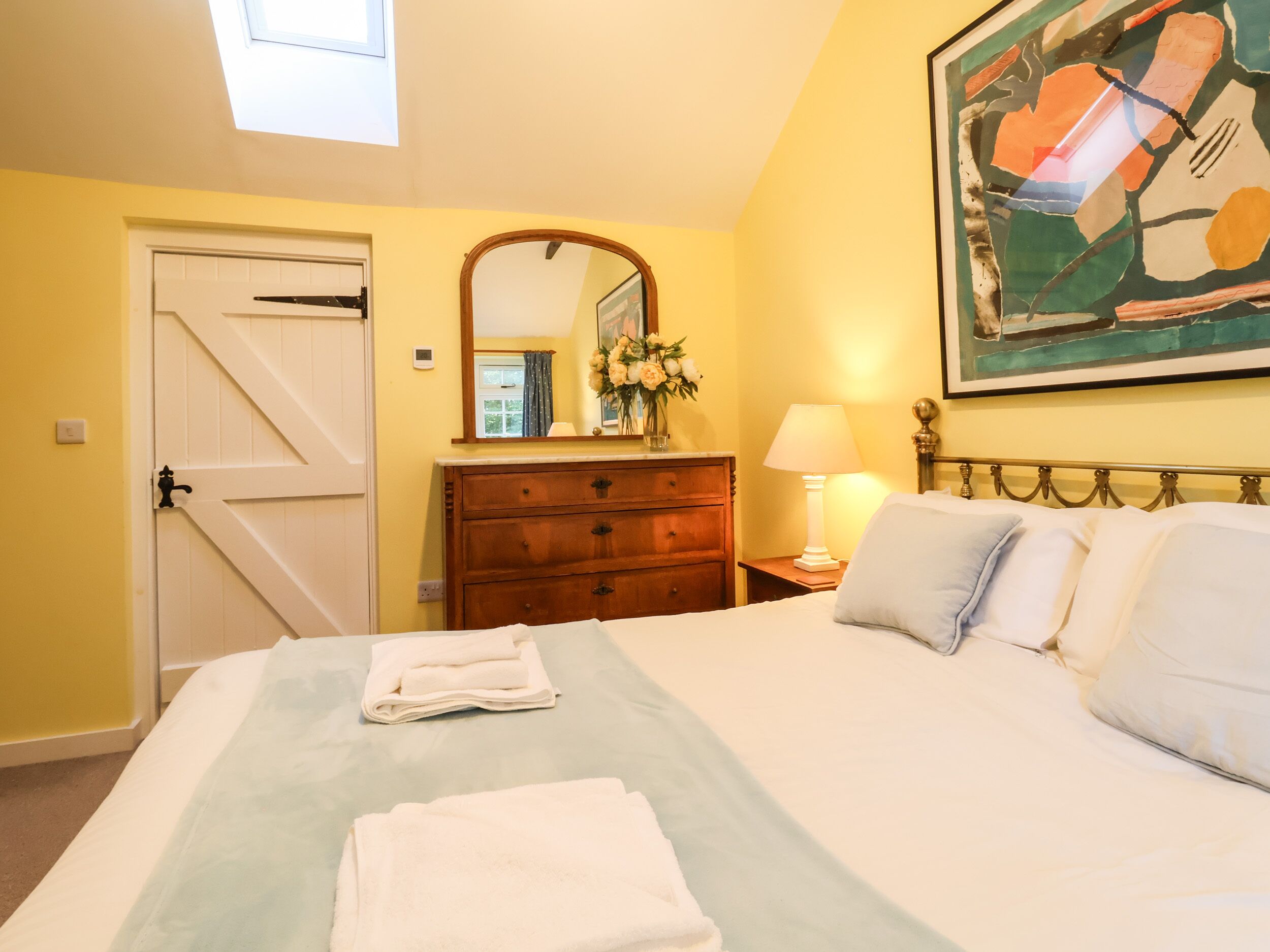 A hotel room with a bed, a dresser, a mirror, a painting, and a window.
