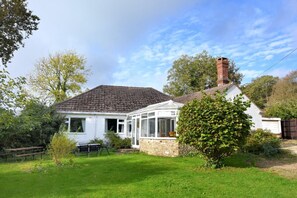 Une maison de plain-pied avec un toit en tuiles, une véranda et un jardin comprenant une pelouse et un petit arbre.
