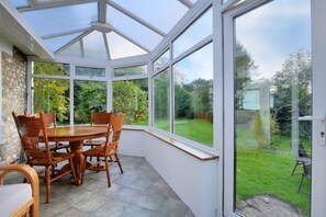 A conservatory with a stone wall, a wooden table, and chairs. - Rooks Acre (Lyme Regis)