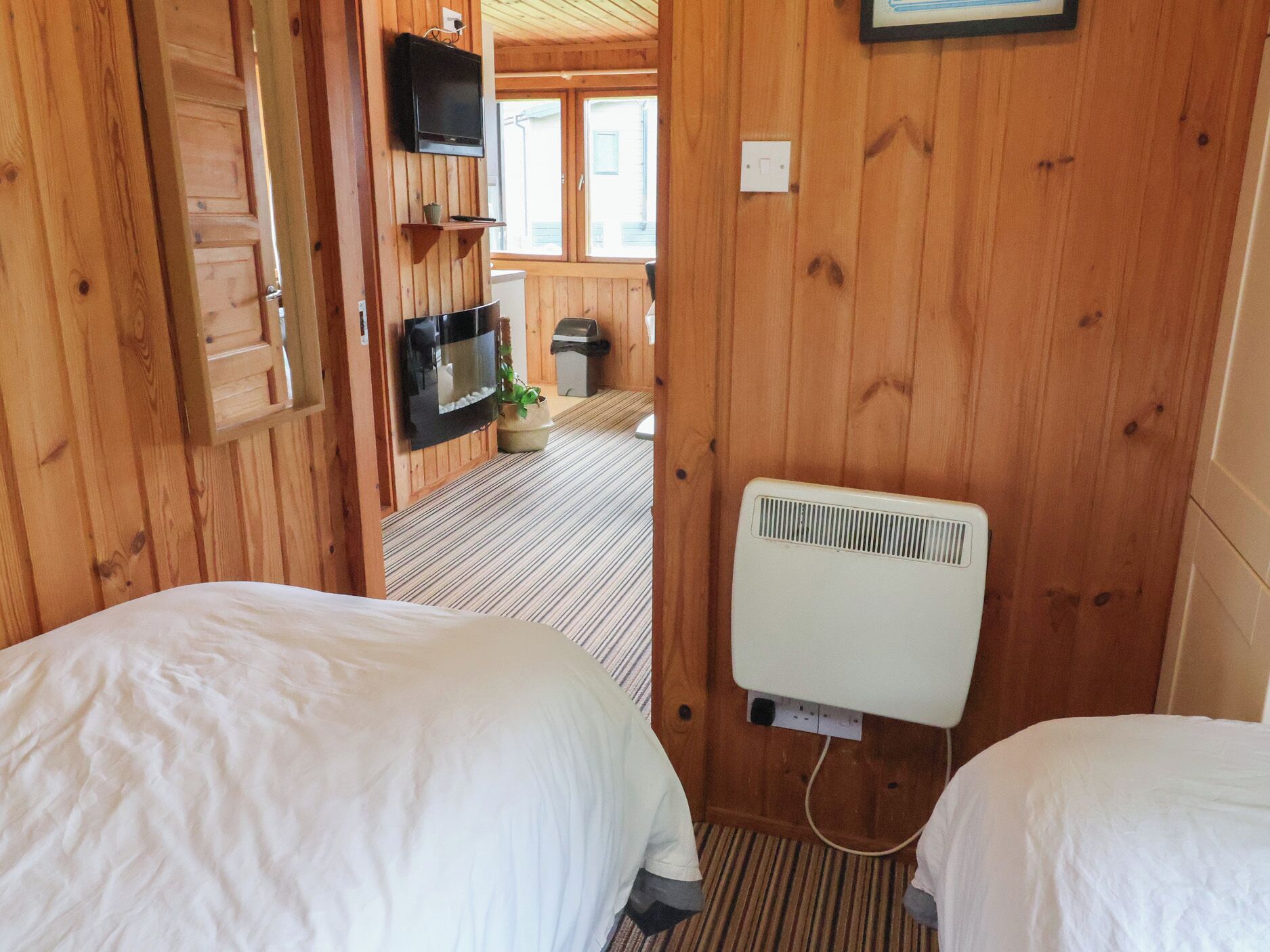 Una habitación con paneles de madera, dos camas, un televisor montado en la pared y un radiador.