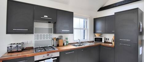A modern kitchen with dark cabinets, a wooden countertop, a gas stove, a microwave, and a window with natural light.