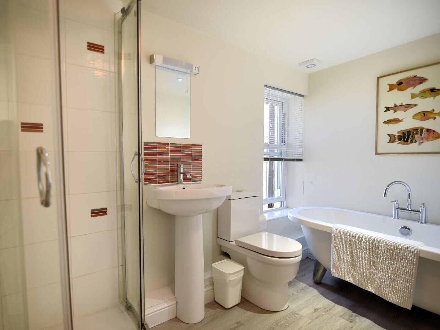 A modern bathroom with a glass shower enclosure, a white sink, a toilet, and a bathtub with a decorative towel.