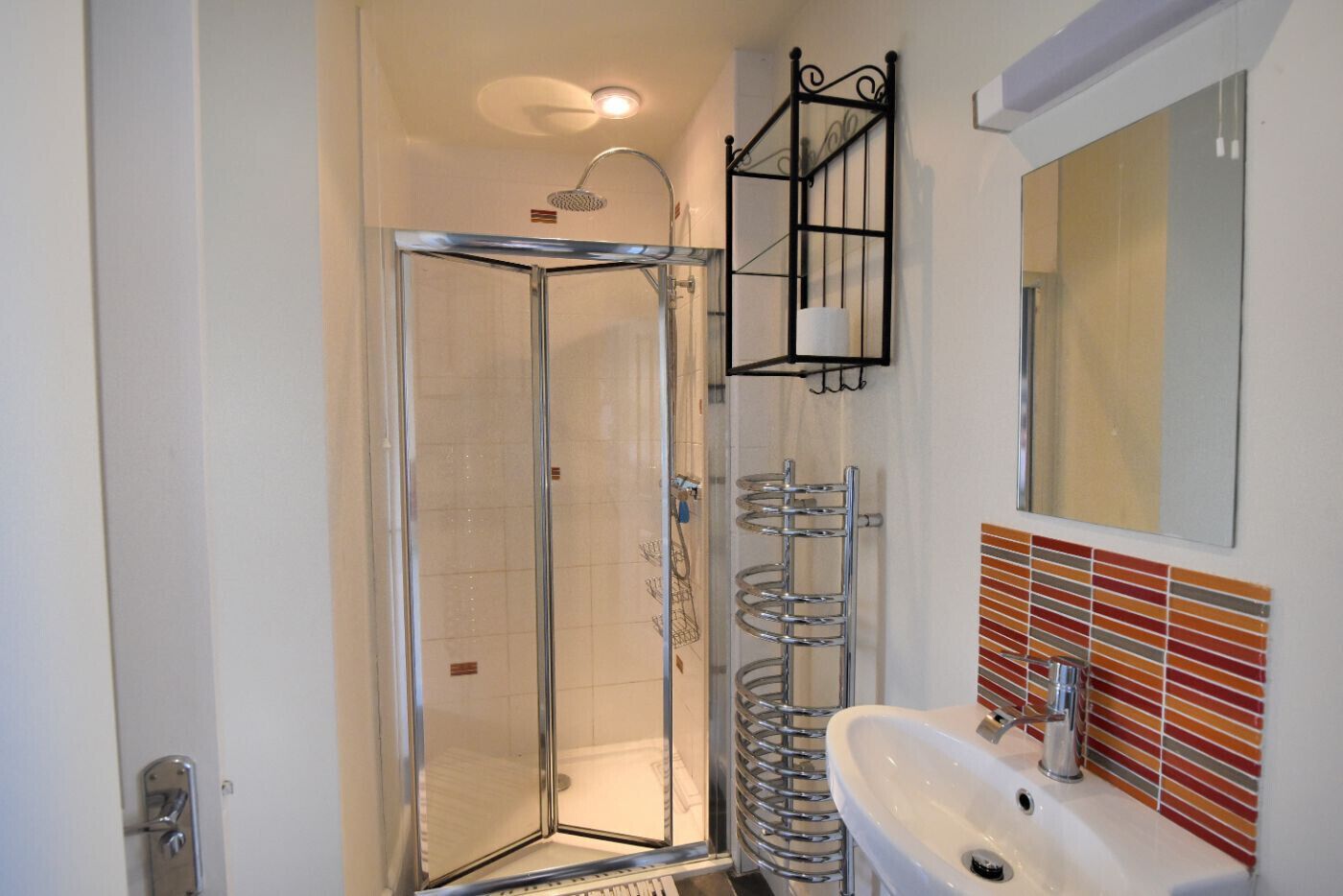A modern bathroom with a glass-enclosed shower, a chrome towel rack, and a tiled backsplash.