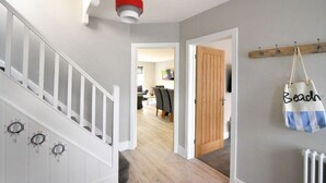 A staircase with white railings and a red light fixture, leading to a room with a wooden door and a wall-mounted bag labeled "Beach". - Lightkeepers Cottage (Lyme Regis)