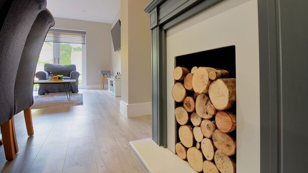 A modern living room with a fireplace, a sofa, and a dining area. - Lightkeepers Cottage (Lyme Regis)