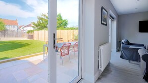A modern living room with a sliding glass door leading to an outdoor patio area. - Lightkeepers Cottage (Lyme Regis)