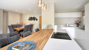 A modern kitchen with white cabinets, a wooden dining table, and a built-in oven. - Lightkeepers Cottage (Lyme Regis)