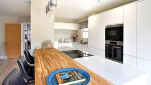 A modern kitchen with white cabinets, a wooden dining table, and a built-in oven. - Lightkeepers Cottage (Lyme Regis)