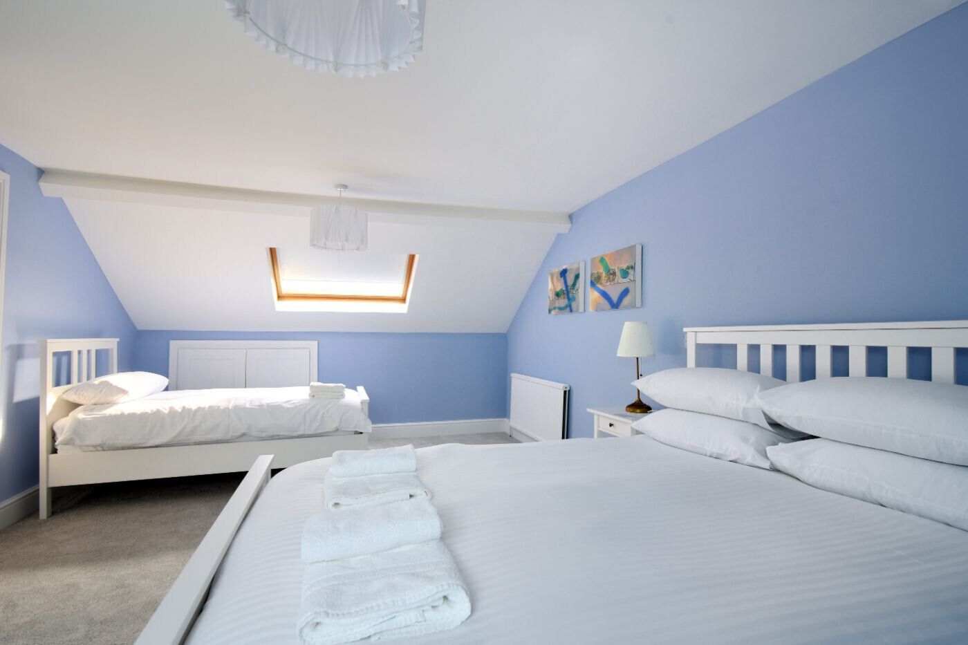A bedroom with two beds, a skylight, a radiator, and artwork on the wall.